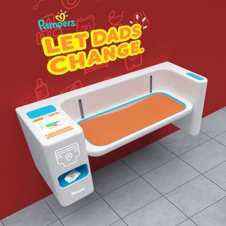 A pampers-branded diaper changing station with the words 'Let dads change' written on the wall above it.
